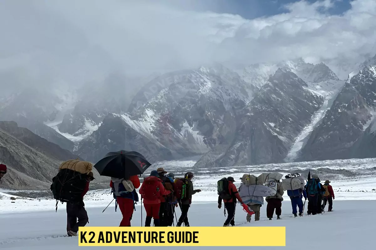 k2-adventure-guide-group-hike Expedition members and porters on a challenging snowy trek in the Karakoram range, with the iconic K2 mountains