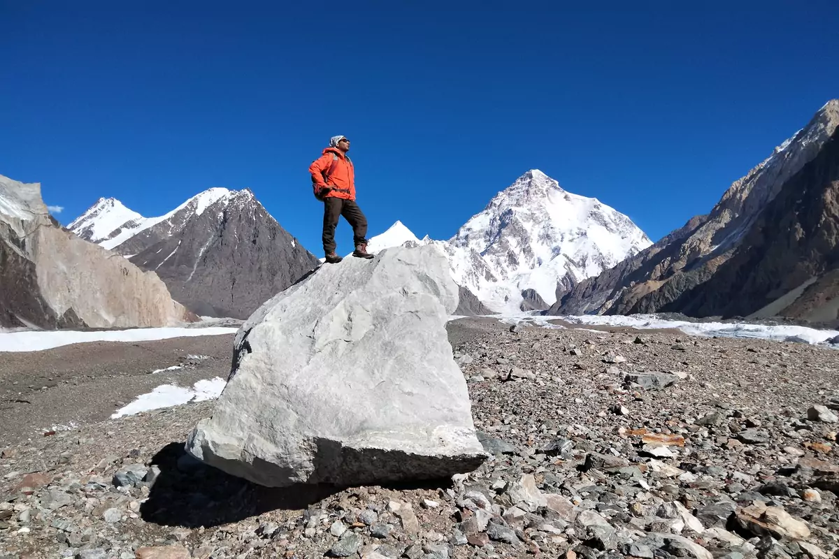 k2-base-camp-trek-pakistan-karakoram A trekker sitting on a rock with a stunning view of K2 in the background during the K2 Base Camp trek